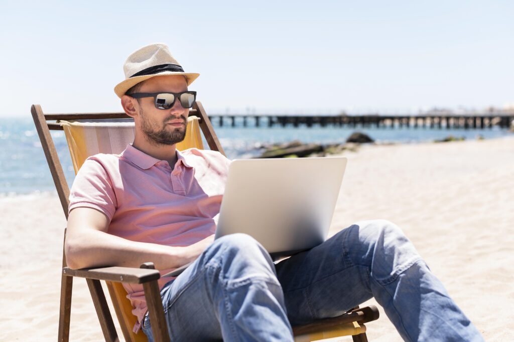 Man working on a laptop from a beach chair, representing income from a short-term rental property